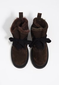 Botines de ante marrón con cordones negros, forro de piel y suelas de goma. Presentan una puntera y una lengüeta de tela en la parte trasera.