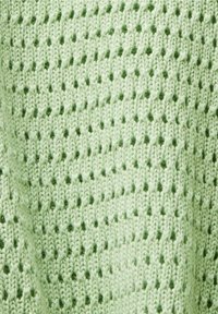 Jasnozielona dzianina z otwartym splotem, z teksturowanymi ściegami i małymi wypukłymi kropkami w całym wzorze.