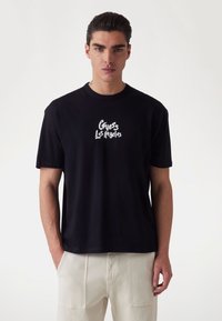 Camiseta de algodón negra con el logo "Guess Los Angeles" en blanco. Corte casual con mangas cortas y escote redondo.