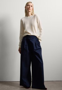 Un pull crème à manches longues associé à un pantalon large bleu marine. Texture douce, coupe décontractée et détails plissés sur le pantalon.