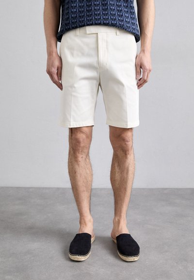 Crème-kleurige shorts met een platte voorkant, zijzakken en een getailleerde pasvorm. Gecombineerd met zwarte suède espadrilles en een gebloemd topje.