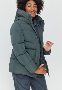 Dark green padded jacket with a high collar, zip closure, and visible stitching. Features a relaxed fit and elastic cuffs.