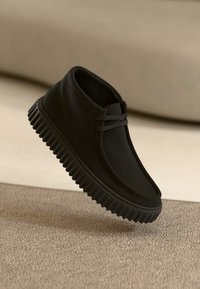 Stivaletto nero con punta rotonda, suola in gomma e parte superiore texturizzata. Presenta una minimal laccatura e una finitura liscia.