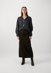 Σκούρο ναυτικό πλεκτό μπολero με υφασματική υφή και τρία λευκά κουμπιά, σε συνδυασμό με μια μακριά σκούρα καφέ τζιν φούστα και μαύρες μποτάκια μέχρι τον αστράγαλο.