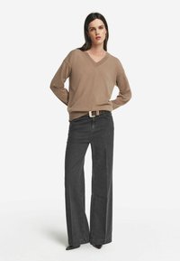 Beiger V-Ausschnitt-Pullover kombiniert mit grauen weiten Jeans. Der Pullover hat eine weiche Textur, während die Jeans eine strukturierte Passform und ein schmal zulaufendes Bein aufweisen.