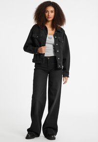 Black denim jacket with front pockets and silver buttons, worn over a gray tank top, paired with wide-leg black jeans and black platform boots.