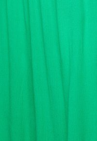 Jasnozielony materiał o gładkiej, teksturowanej powierzchni. Tkanina wykazuje subtelne różnice i delikatne fałdy, odbijając światło.