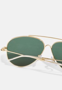 Kulta aviator-aurinkolasit vihreillä linsseillä, joissa on kaksoisjousirakenne ja läpinäkyvät yksityiskohdat tempoissa.