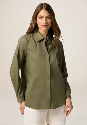 Camicia verde oliva a maniche lunghe con colletto, bottoni frontali e vestibilità leggermente ampia. Tessuto morbido con una finitura lucida.