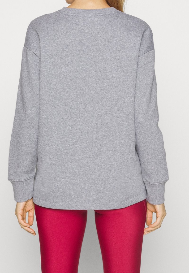 Personne portant un sweat-shirt gris uni à manches longues et des leggings rose vif, vue de dos sur fond blanc.