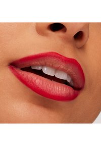Gros plan sur des lèvres avec du rouge à lèvres rouge et une bouche légèrement entrouverte montrant des dents blanches et une partie du nez au-dessus.