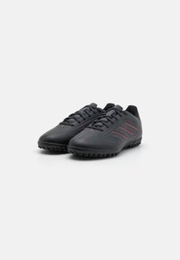 Black soccer shoes with a textured surface, featuring red accent stripes and a rubber outsole designed for traction on grass surfaces.