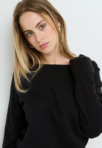 Maglione nero a maglia con scollatura ampia e maniche lunghe, caratterizzato da una texture morbida. Il tessuto sembra leggero e si drappeggia comodamente.