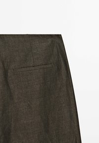 Mörkgrå byxor utställda, med en slät textur, en bakficka med horisontell spricka och minimalistiska designelement.
