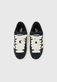 Black and gray Adidas sneakers with white laces, displayed from above on a light background, featuring the iconic three stripes design.