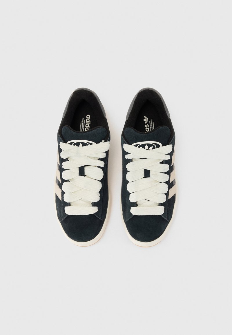 Zapatillas Adidas en negro y gris con cordones blancos, exhibidas desde arriba sobre un fondo claro, con el icónico diseño de las tres rayas.