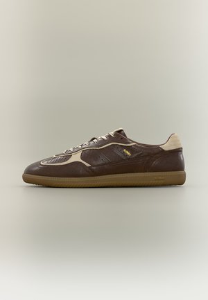 Baskets basses en cuir marron avec des touches beige, des lacets beiges et une semelle en gomme sur un fond clair uni.