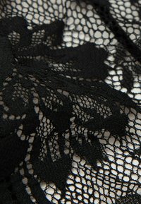 Tissu en dentelle noire avec un motif floral, présentant un tissage délicat et texturé ainsi que des zones en maille ouverte, mettant en valeur des détails et un design sophistiqués.