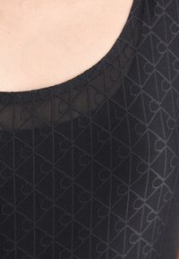 Crna majica bez rukava s okruglim izrezom, s geometrijskom teksturom međusobno isprepletenih trokuta i krugova. Tkanina izgleda lagano i prozračno.