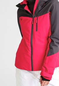 Giacca da sci rosa e nera con un design aderente, tasche con zip e colletto alto. Realizzata in materiale impermeabile, presenta dettagli testurizzati.