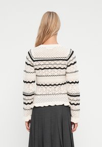 Sweter w kolorze kremowym, wykonany na drutach, z czarnymi paskami, teksturowymi detalami, falbanowym wykończeniem i długimi rękawami, zestawiony z ciemnoszarym spódnicą.