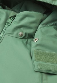 Zelená zateplená bunda má textúrovanú tkaninu, zips, patentky a suchý zips na golieri.