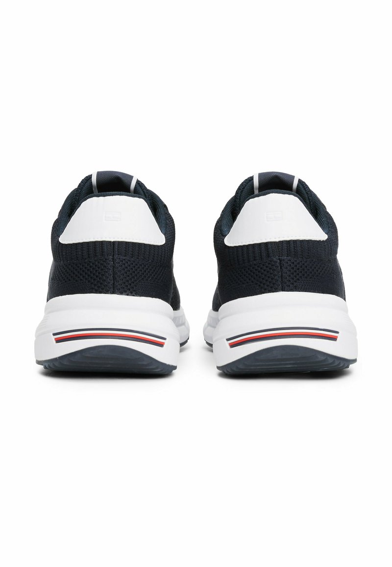 Zapatillas deportivas de punto en color azul marino con acentos en blanco, diseñadas con una suela acolchada, que cuentan con un talón texturizado y detalles rayados en la suela.