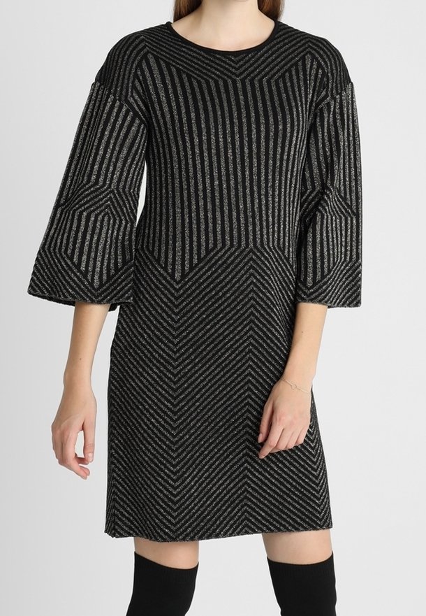 Femme portant une robe rayée noire et argentée longueur genou avec des manches trois-quarts évasées et des chaussettes noires hautes jusqu'aux genoux.