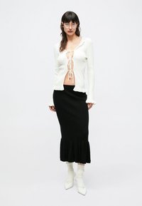 Balta, siaurais ilgarankovė latelinė su priekine raištelių detale ir raukiniais, derinama su juoda megzta midi sijonu su praplatintu kraštu. Baltos aukštakulnės aulinės batai.