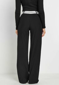 Zwarte wijde broek met een soepele textuur, voorzien van een witte gestreepte tailleband en riemlussen, ontworpen voor een comfortabele pasvorm.