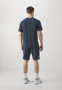 Marineblaue Sport-T-Shirt und Shorts, aus leichtem Material, mit lockerer Passform. Weiße Logoakzente und kontrastierende Seitenpaneele sichtbar.