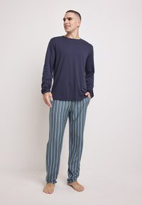 Camisa de manga larga de color marino combinada con pantalones de pijama a rayas verdes y azules. Tejido suave, corte relajado y puños en los tobillos de los pantalones.