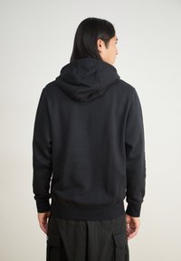 Felpa nera con un ampio cappuccio regolabile. Realizzata in tessuto morbido, con orlo e polsini a coste, progettata per una vestibilità comoda.