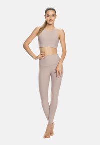 Sportni modrček in hlače v svetlo bež barvi. Tkanina je gladka in prilegajoča, brezšivna zasnova in visok pas zagotavljata udobje.