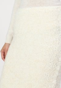 Jupe tricotée blanche en tissu texturé et pelucheux. Présente une coupe mi-longue et une taille côtelée. Apparence douce et cozy.