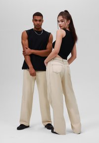 Black sleeveless top paired with light beige wide-leg pants; subtle stitching detail and side pockets; plain black shoes.