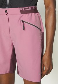 Roze sport shorts met een donker bordeauxrode tailleband. Voorzien van een ritszak aan de zijkant, geperforeerde details en een gladde textuur.