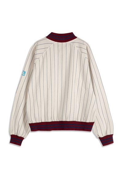 Veste blanche à fines rayures noires verticales, col, poignets et ceinture côtelés bordeaux et marine, avec un écusson logo bleu sur la manche gauche.