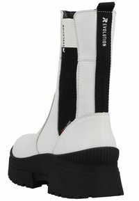 White leather ankle boots with a chunky black sole, featuring elastic side panels and a logo on the pull tab, designed for easy wear.