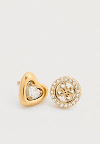 Σκουλαρίκια καρφί από χρυσό τόνο με σχέδιο σε σχήμα καρδιάς, κεντρική διαφανή πέτρα και στρογγυλό δίσκο με κυκλικά διακοσμητικά από πέτρες.
