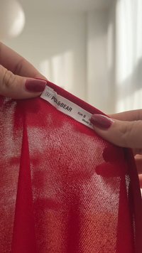 Czerwona, przezroczysta tkanina trzymana w dłoniach, z białą metką zawierającą napis "PULL&BEAR" oraz informacje o rozmiarze, podkreślająca swoją lekką teksturę.
