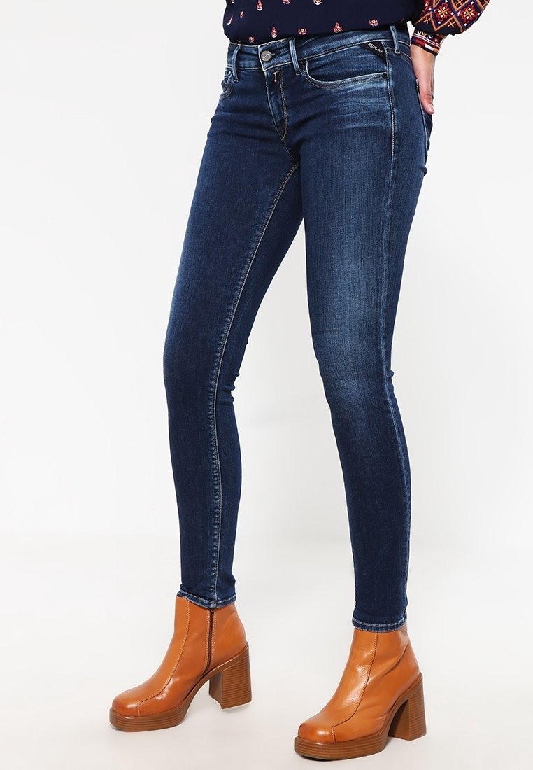 Jeans ajustados en denim azul oscuro, con una cintura alta, diseño de cinco bolsillos y desvanecidos sutiles. Combinados con botas de tobillo de plataforma marrones.