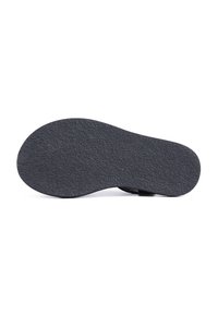 Semelle texturée noire d'une sandale plate vue par le dessous sur un fond blanc.