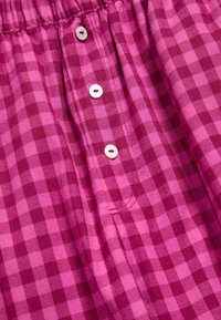 Różowa kratkowana tkanina w wzór siatki, z białymi guzikami z przodu i elastycznym paskiem w talii dla wygody.