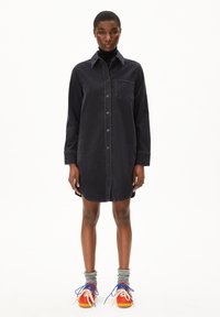 Dunkelblaues Corduroy-Hemdkleid mit Knopfleiste, langen Ärmeln, Kragen und Brusttasche. Kombiniert mit bunten Sneakers und grauen Socken.