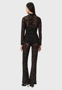 Black lace jumpsuit with long sleeves and flared legs, featuring floral pattern and sheer texture; includes a back zipper closure.