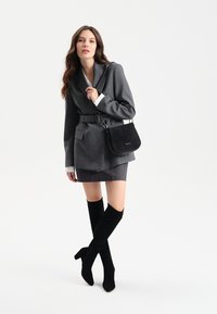 Szary żakiet dopasowany z paskiem, w połączeniu z szarym mini spódnicą i czarnymi wysokimi botkami na obcasie. Czarna torebka na ramię.