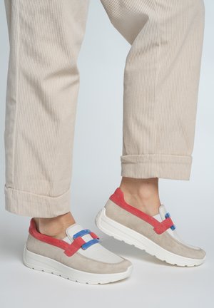 Beige corduroy pants cuffed above ankles, worn with beige sneakers featuring red straps and blue buckles on white soles.