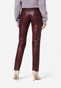 Bordeauxfarbene Lederhose mit schmaler Passform, ausgestattet mit Gesäßtaschen und Kniefalten, kombiniert mit weißen High Heels.