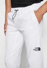 Vita, lätta joggers med elastisk midja och svart dragsnöre. Har två sidofickor och en svart logotyp på det nedre benet.